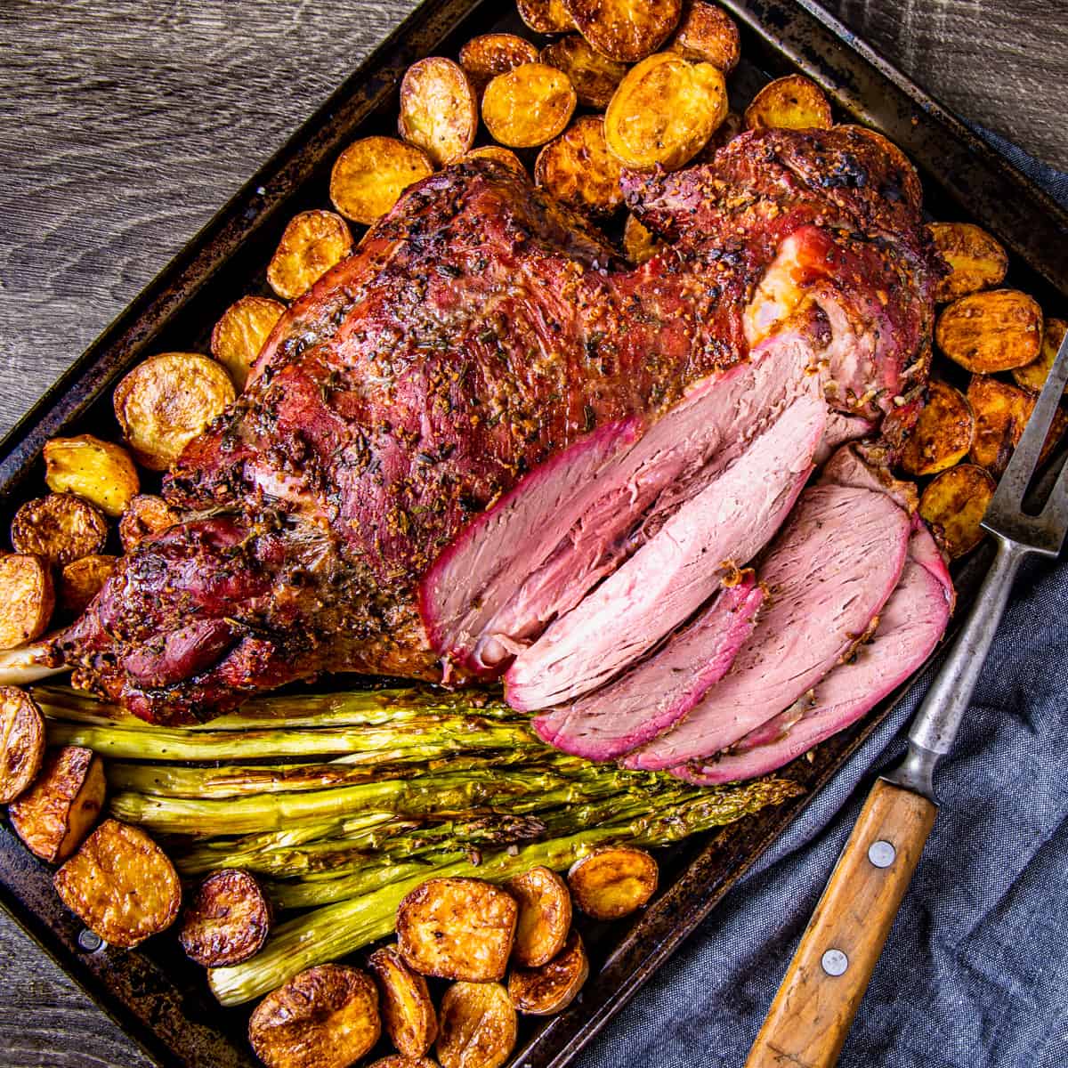 smoked leg on lamb, partially sliced surrounded in potatoes.